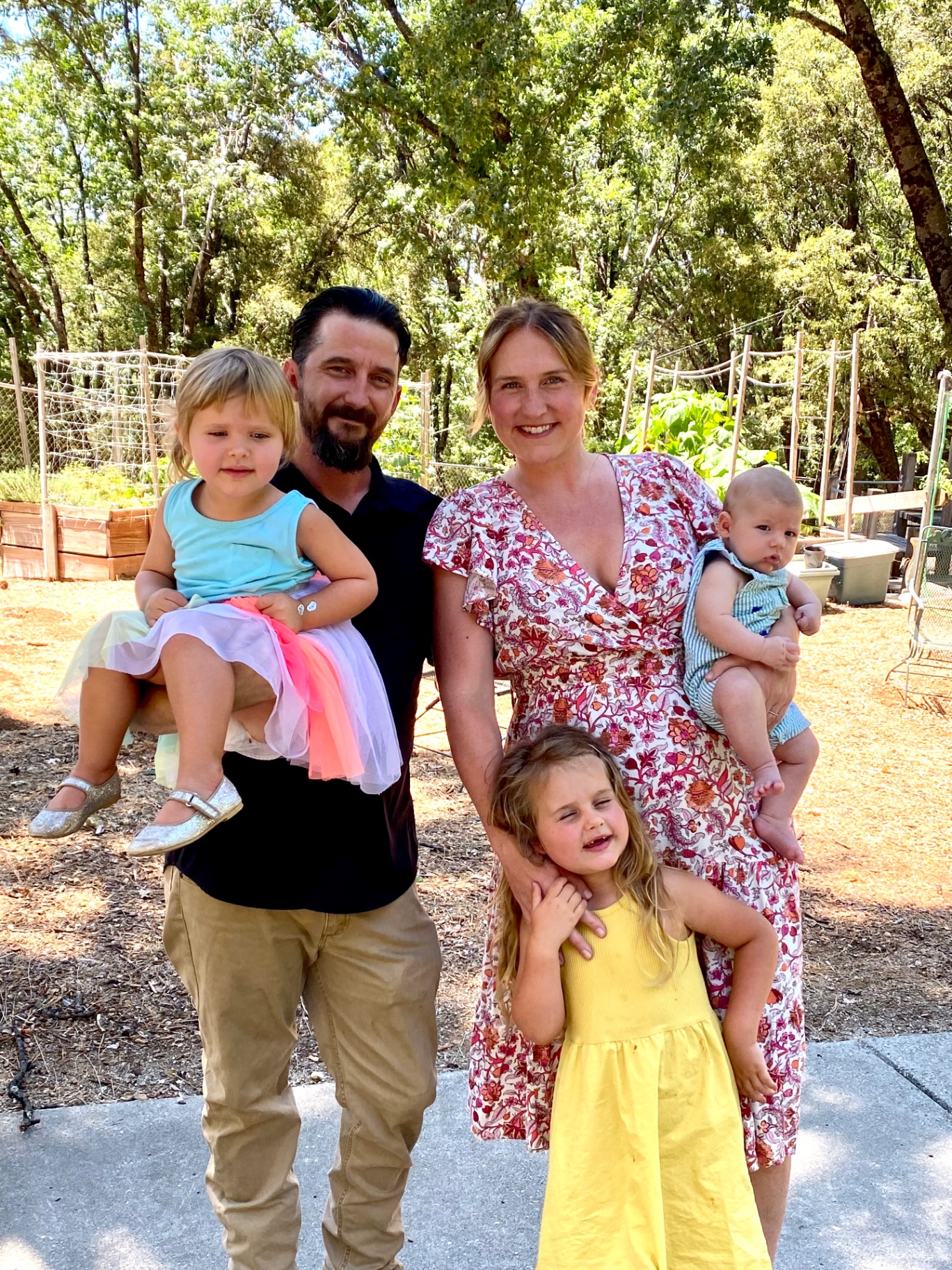 The Estey family — mom, dad, and their three little ones — standing in the garden surrounded by oak trees and trellises