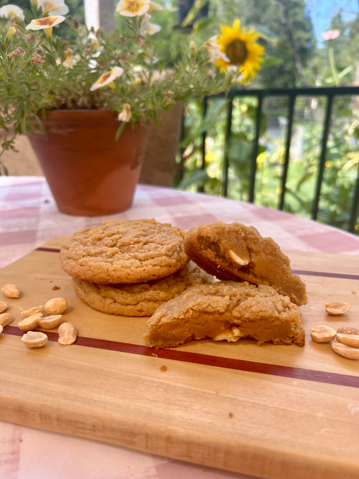 A stack of thick bakery-style peanut butter cookies on a wooden board, one broken to show a soft golden interior and whole peanuts