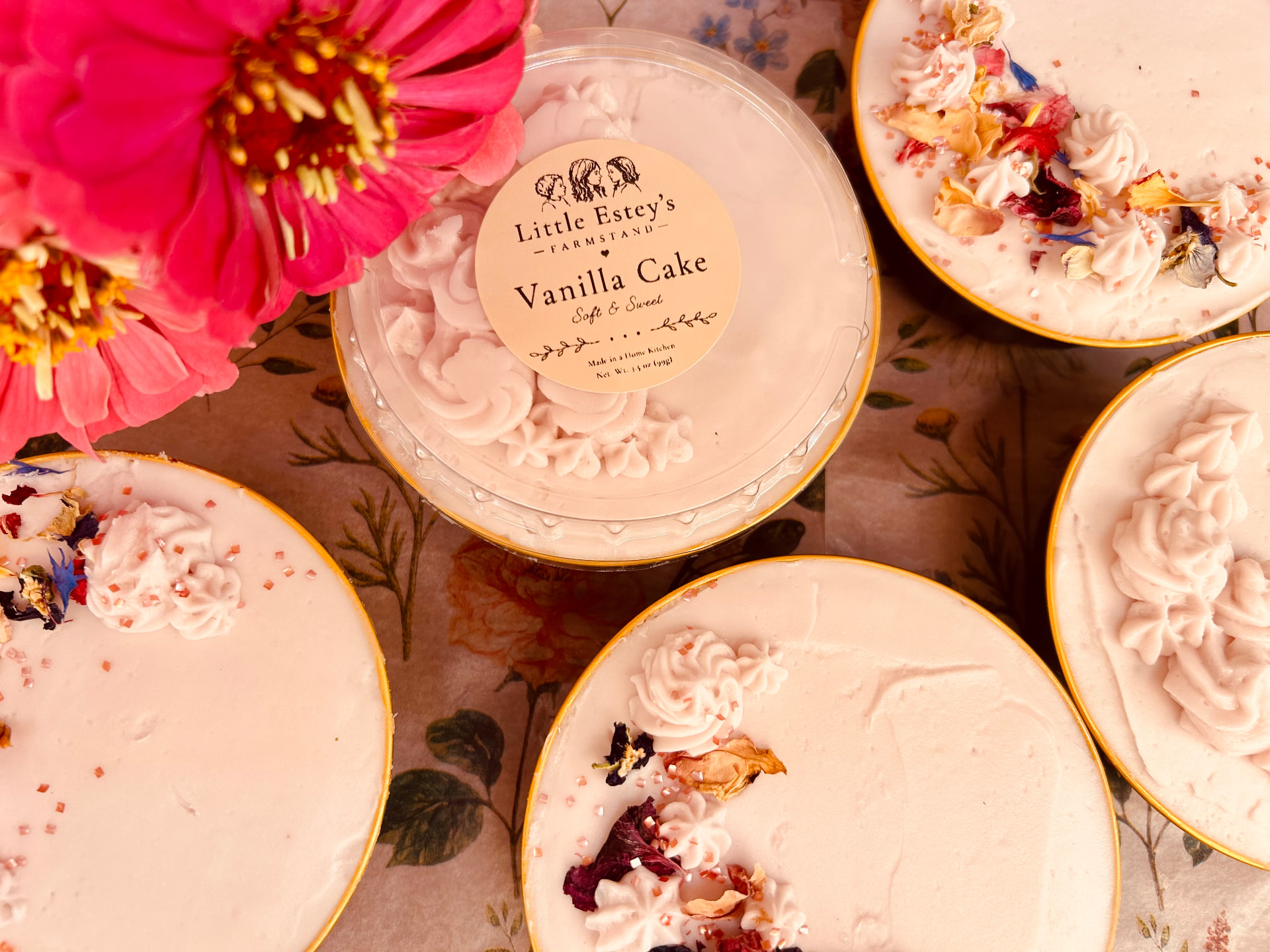 Small vanilla cake jars with pale pink frosting and dried flower petals, labeled Little Estey's Farmstand Vanilla Cake